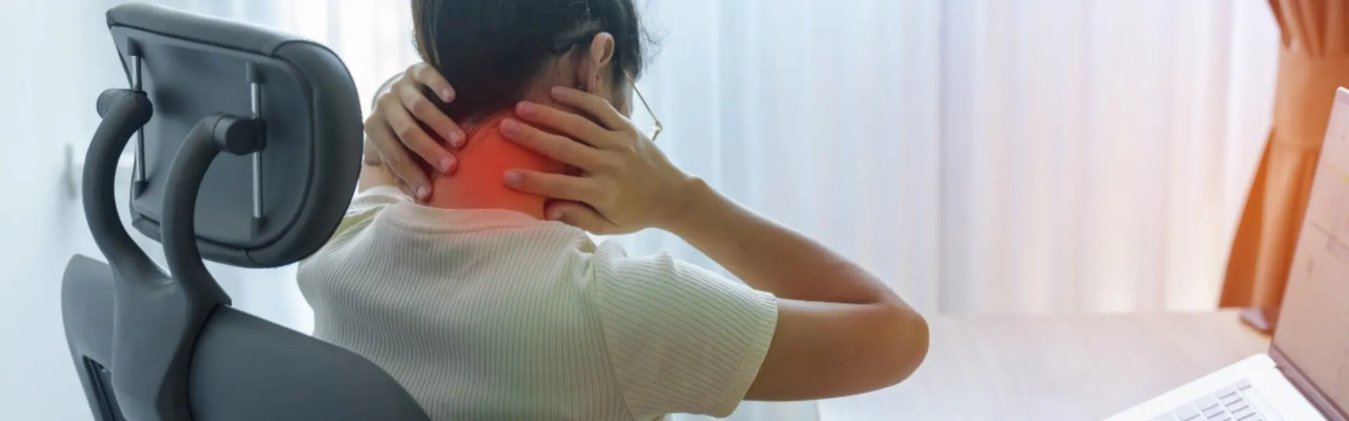 Mujer con dolor de cuello y espalda debido a fibromialgia trabajando en computadora.