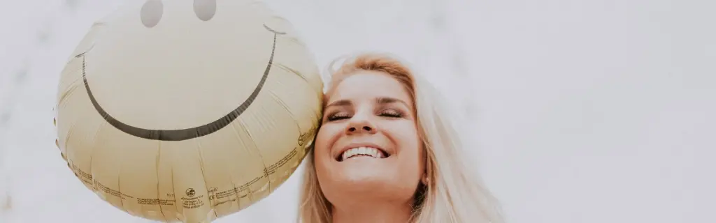 Mujer feliz con un globo sonriente representando la psicología positiva y el bienestar